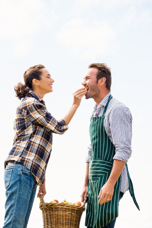 Smiling young woman feeding apple to man against skyの写真素材