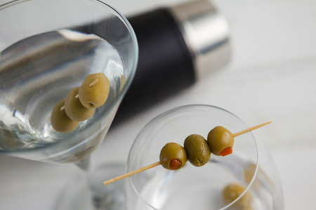 Close up of olives in vodka martini with cocktail shaker in backgroundの写真素材