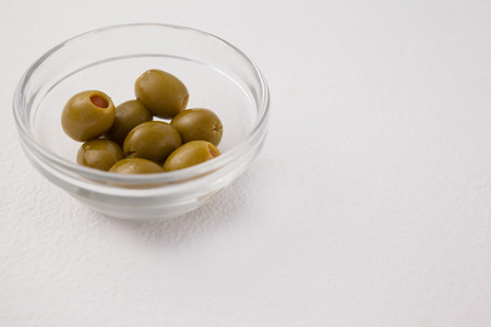 High angle view of green olives in glass bowl on white tableの写真素材