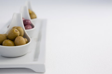 Close up of black and green olives in containers on tray against white backgroundの写真素材