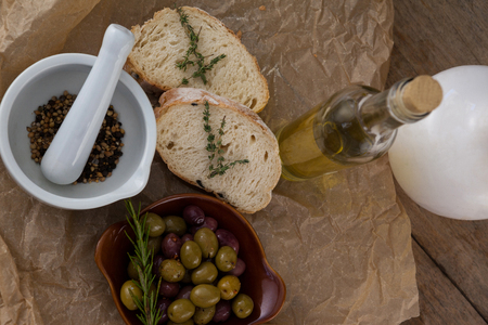 Directly above shot of olives with oil bottle and bread by spices in mortar pestle on crumbled paper at tableの写真素材