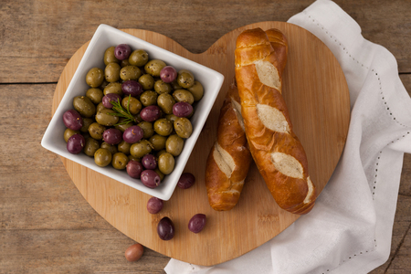 Olives in container by bread on heart shape cutting board with napkinの写真素材