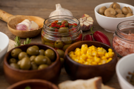 Olives and corns in bowl by spices on tableの写真素材
