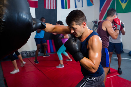 Young male boxer punching bag in fitness studioの写真素材