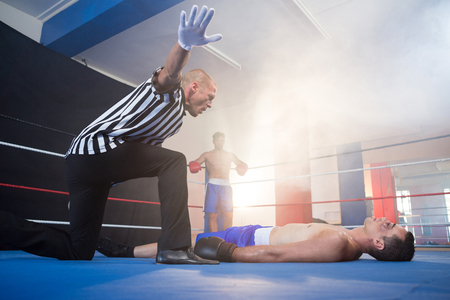 Referee gesturing by unconscious male boxer lying in boxing ring at fitness studio
