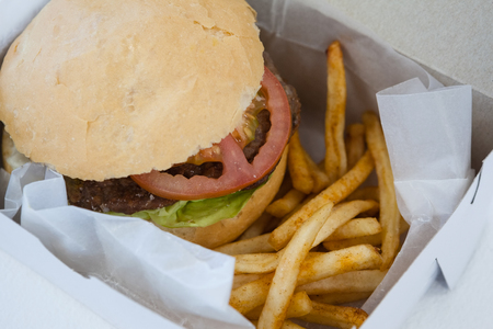 Close-up of hamburger and french fries in a take away container on table