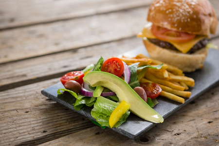 Close up of salad with french fries and burger on slate at tableの写真素材