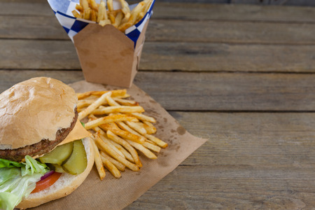 Close-up of hamburger and french fries in take way bag on wooden tableの写真素材