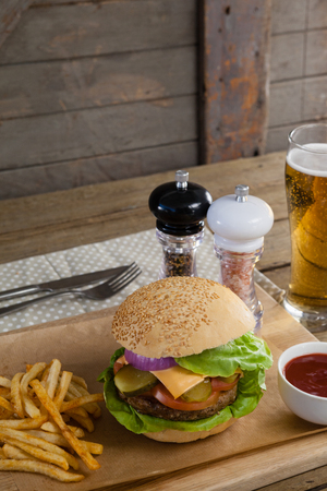 Close-up of hamburger, french fries, tomato sauce and glass of beer on chopping boardの写真素材