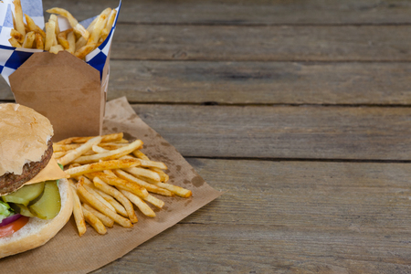 Close-up of hamburger and french fries in take way bag on wooden tableの写真素材