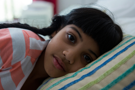 Close-up portrait of girl lying on bed at homeの写真素材