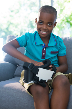 Portrait of smiling boy adjusting virtual reality headset while sitting on sofa at homeの写真素材