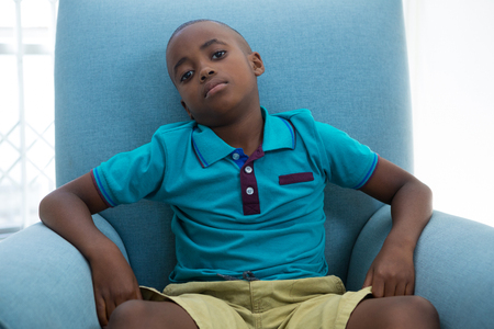 Portrait of boy sitting on blue armchair in living room at homeの写真素材