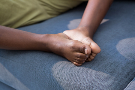 Low section of boy joining feet while sitting on gray sofa in living room at homeの写真素材