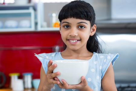 Portrait of smiling girl holding bowl in kitchenの写真素材