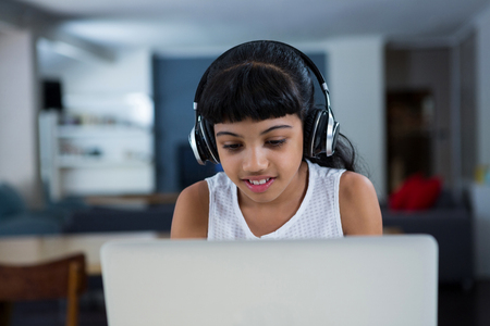 Girl using laptop while listening music from headphones at homeの写真素材