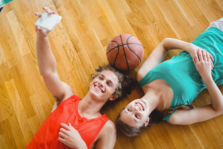 Overhead view of man taking selfie while lying with female friend on hardwood floor in courtの写真素材