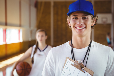 Portrait of smiling male coach with basketball player standing in courtの写真素材