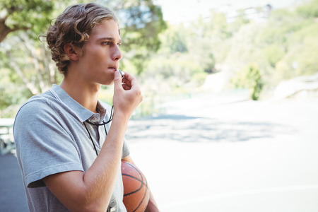 Man with basketball whistling while standing in basketball courtの写真素材