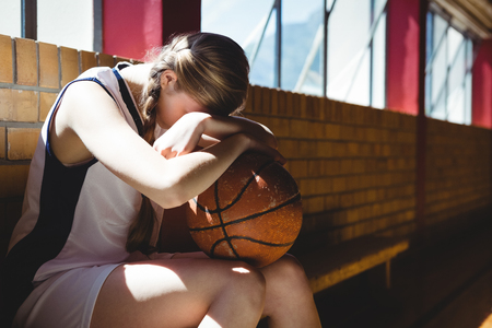 Tired basketball player sitting by window in courtの写真素材