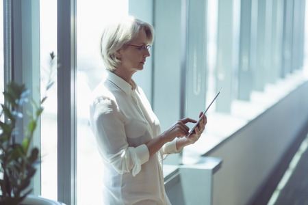 Businesswoman woman using tablet computer while standing by windowの写真素材