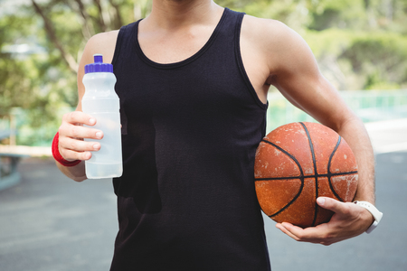 Midsection of  basketball player with holding bottle while standing in courtの写真素材