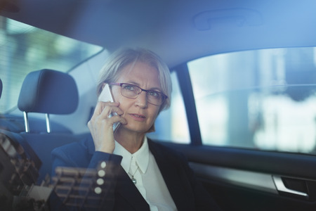 Businesswoman talking on phone while traveling in carの写真素材