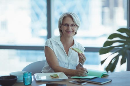 Portrait of businesswoman having food while working at table in officeの写真素材