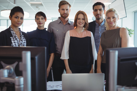 Portrait of young business colleagues standing together by desk at officeの写真素材