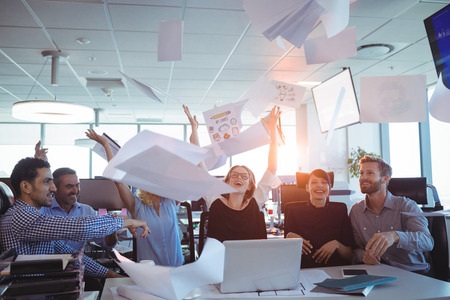 Happy business people tossing papers in air at deskの写真素材