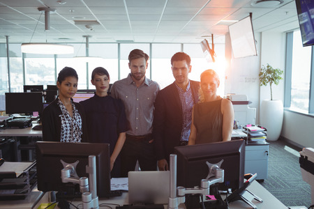 Portrait of business colleagues standing together by desk at office