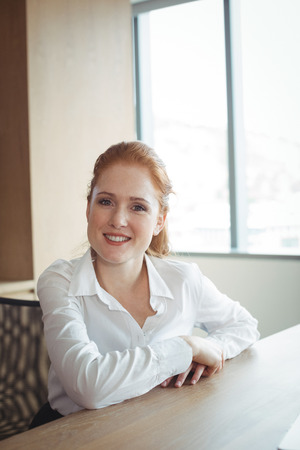 Portrait of smiling businesswoman sitting at desk in officeの写真素材