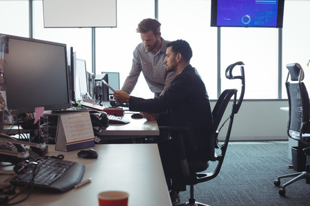 Male business colleagues discussing over documets at desk in officeの写真素材