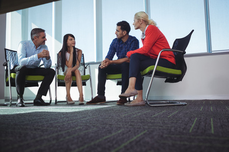 Business colleagues communicating while sitting on chairs by window at officeの写真素材