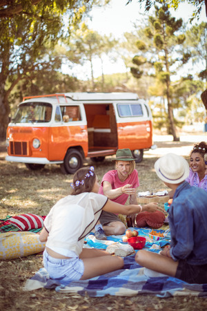 Friends having food during picnic at field on sunny dayの写真素材