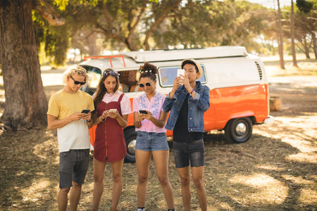 Friends using smart phone while standing on field against camper van