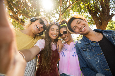 Portrait of smiling friends standing side by side against trees on sunny dayの写真素材