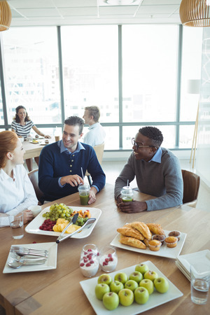 High angle view of smiling business colleagues having breakfast on table at office cafeteriaの写真素材