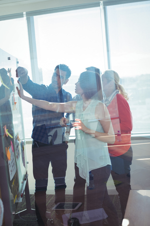 Business entrepreneurs seen through glass discussing over whiteboard at officeの写真素材