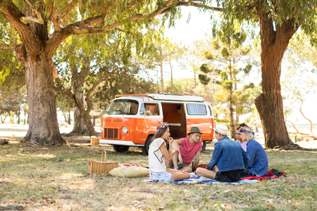 Friends sitting against camper van on field during picnicの写真素材