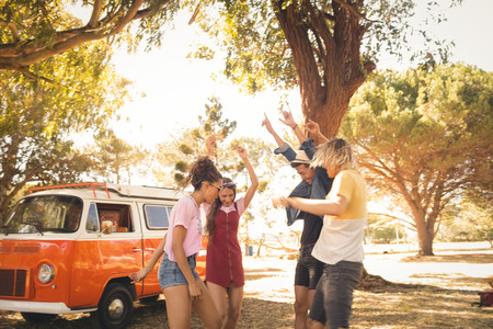 Happy friends dancing on field against camper vanの写真素材