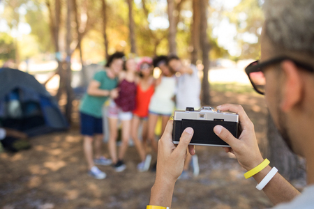 Cropped image man photographing friends while standing at campsiteの写真素材