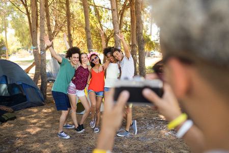 Man photographing cheerful friends while standing at campsiteの写真素材