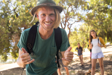 Portrait of man with backpack gesturing with friends in backgroundの写真素材