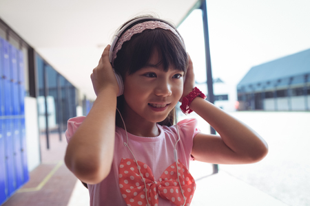 Smiling girl listening music through headphones while standing in corridor at schoolの写真素材