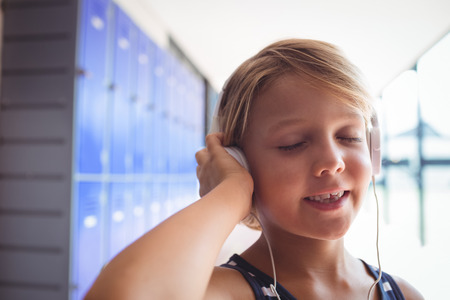 Elementary student with eyes closed listening music through headphones while standing in corridor at schoolの写真素材