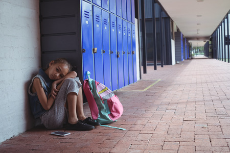 Full length of elementary schoolgirl resting by lockers in corridor at schoolの写真素材