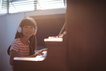 Portrait of smiling girl wearing headphones while practicing piano in classroom at music schoolの写真素材