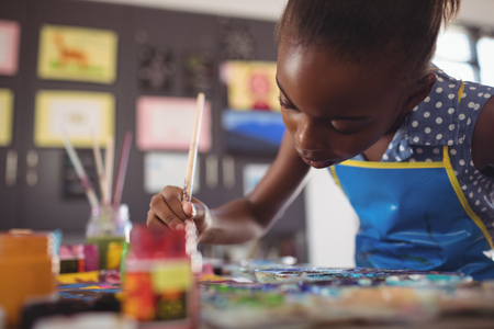 Concentrated elementary girl painting at desk in classroomの写真素材