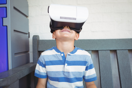 Boy watching virtual reality glasses while sitting on bench at school